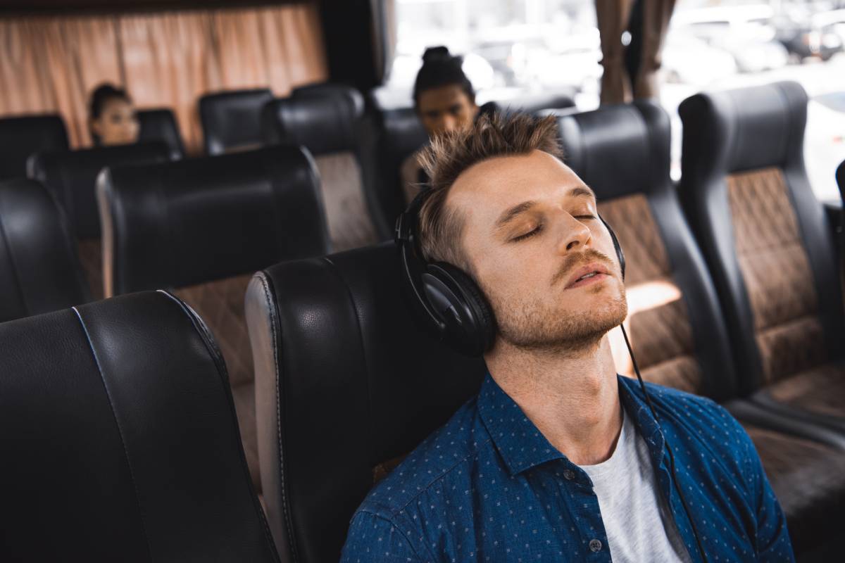 adult man in headphones listening music and sleeping during trip on bus