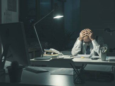 Stressed business executive sitting at desk and working overtime at night, he is overworked and tired