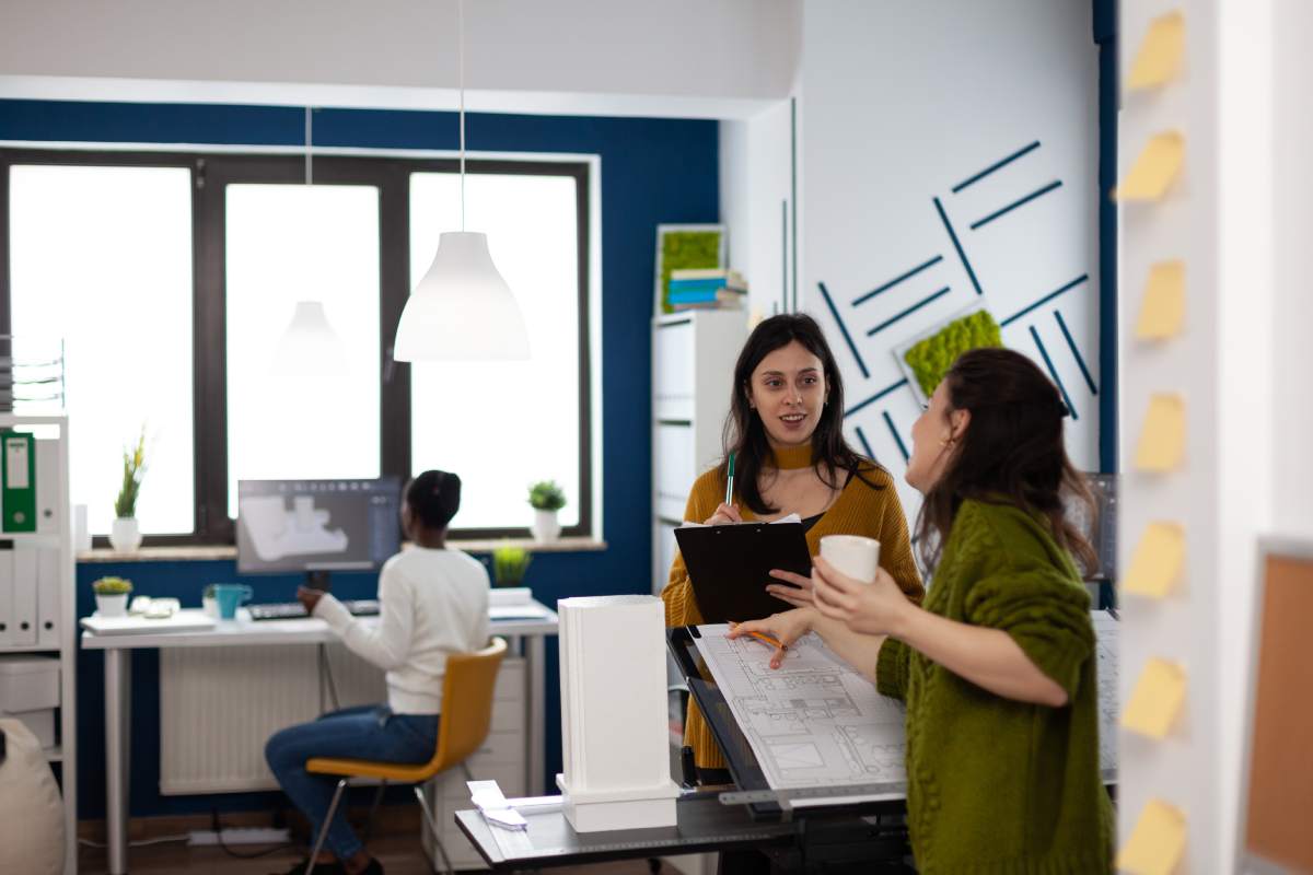 Team of businesswomen standing in creative studio office discussing and analysing building model measuring prototype with pencil. Collegues planning construction ideas design in multimedia workplace