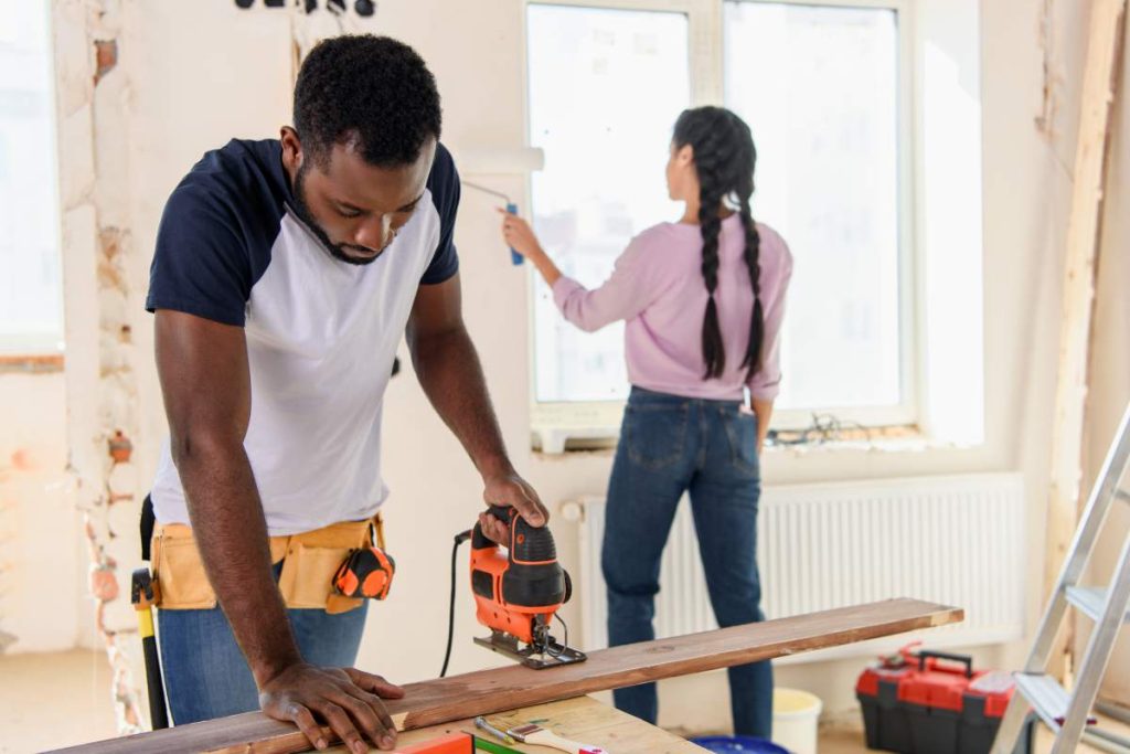 handsome african american man working with jigsaw while his girlfriend working behind during