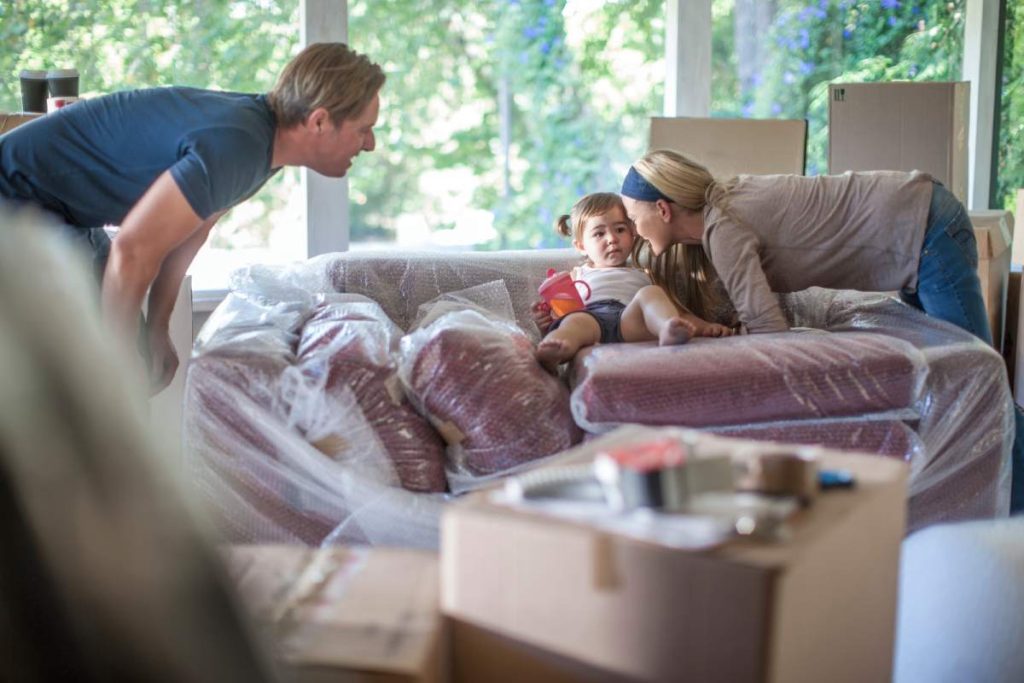 Moving house: young girl sitting on bubble wrapped sofa