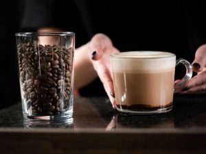 Female barista's hand holding rich mocha coffee in a glass cup. Perfect blend of espresso, cream and chocolate.