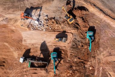 Aerial view road motor grader flatting dirt road surface, Motor grader road construction grader industrial machine construction site new road, Aerial view group excavator working on construction site.