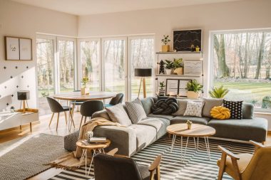 Wooden, round dining table in the corner of an open space living room interior with nordic furniture and decor