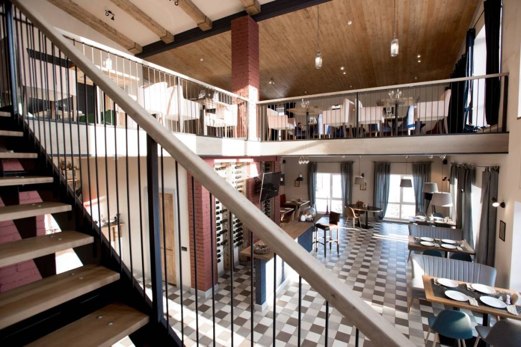 Empty modern fashionable cozy restaurant with staircase and unique furniture, panoramic windows with blue curtains and served tables in cafe